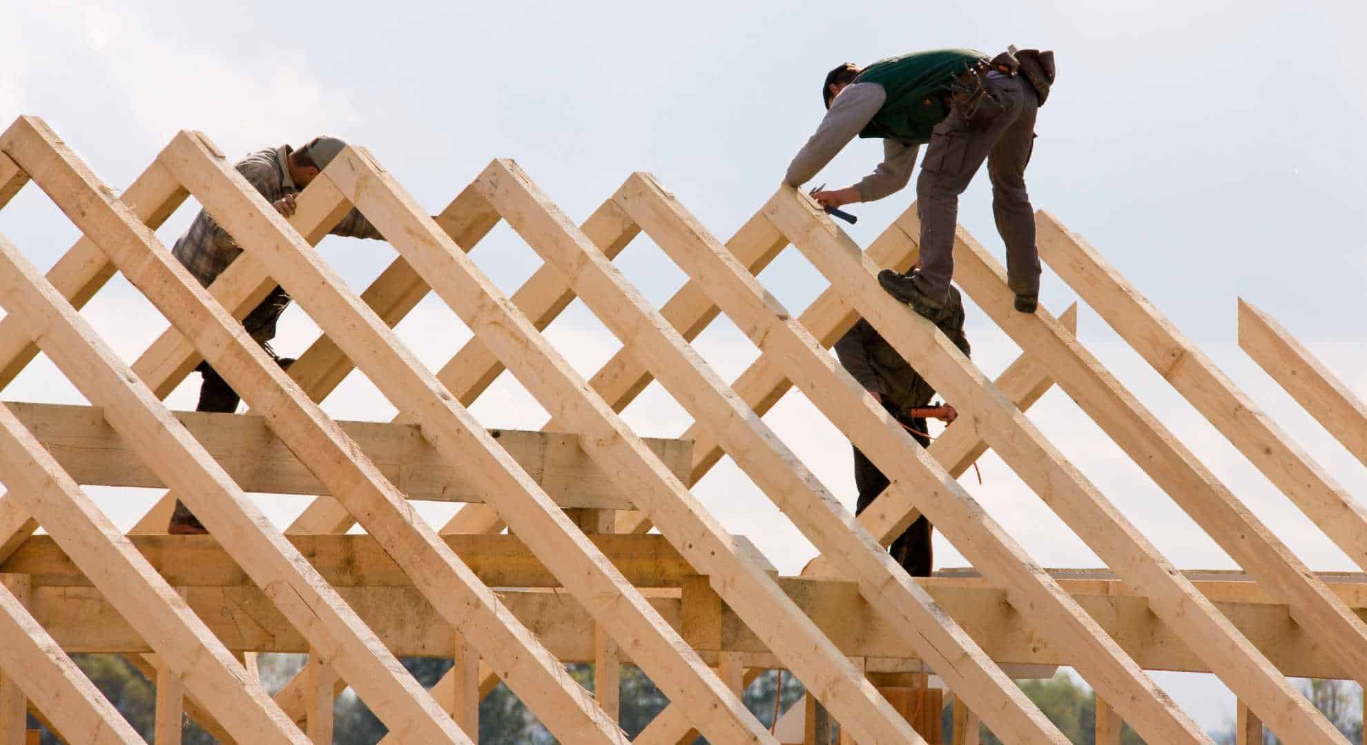 Drachnackt.jpg Zwei Handwerker montieren ein hölzernes Dachtragwerk auf einer Baustelle unter freiem Himmel.