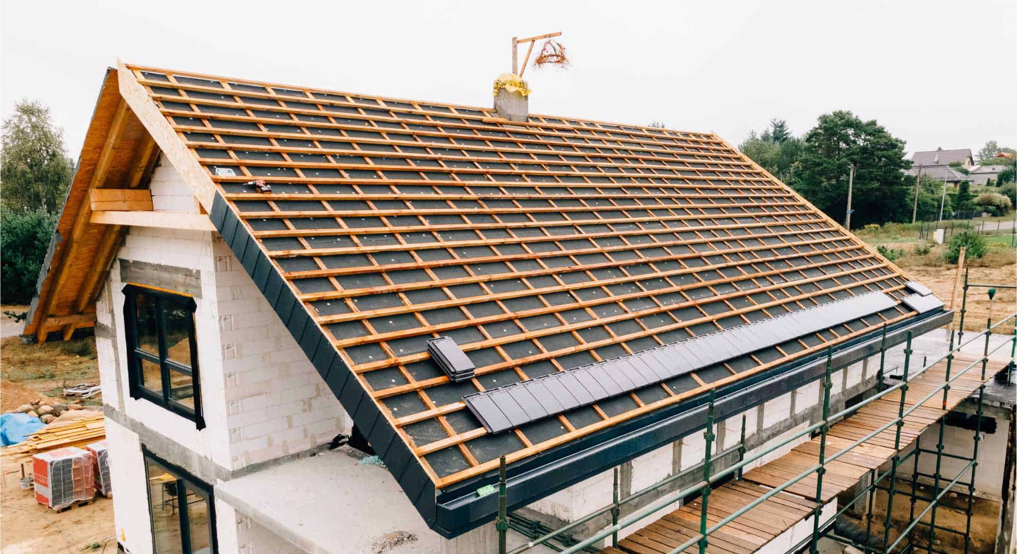 Dachnackt2.jpg Teilweise gedecktes Dach eines Neubaus mit sichtbarer Dachlattung und vorbereiteter Ziegelmontage auf einer Baustelle.