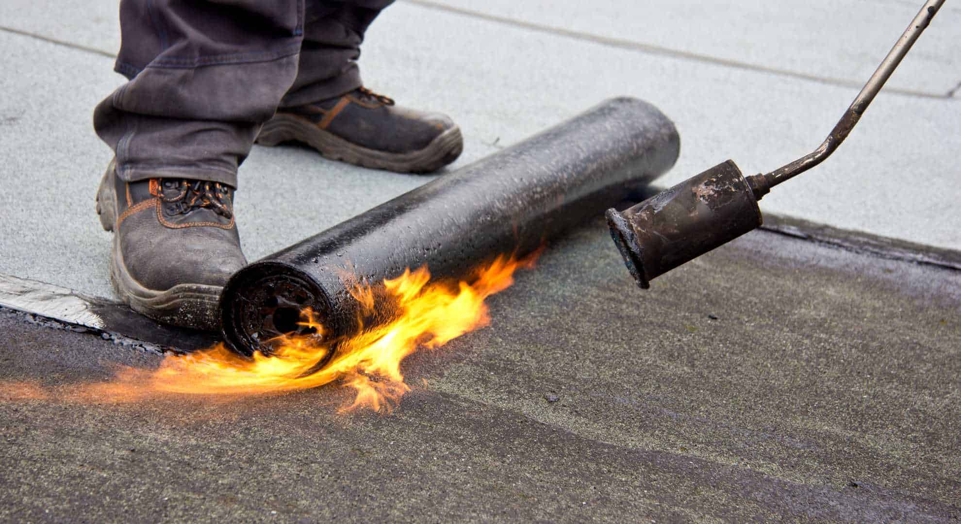 Flachdachneu.jpg Flachdachabdichtung mit offener Flamme – ein Handwerker bringt eine Bitumenbahn mit einem Gasbrenner auf.