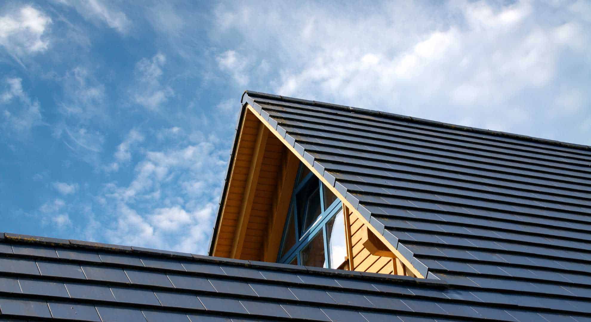 Insterlation.jpg Modernes geneigtes Dach mit neu installierten, glänzenden Dachziegeln unter blauem Himmel.