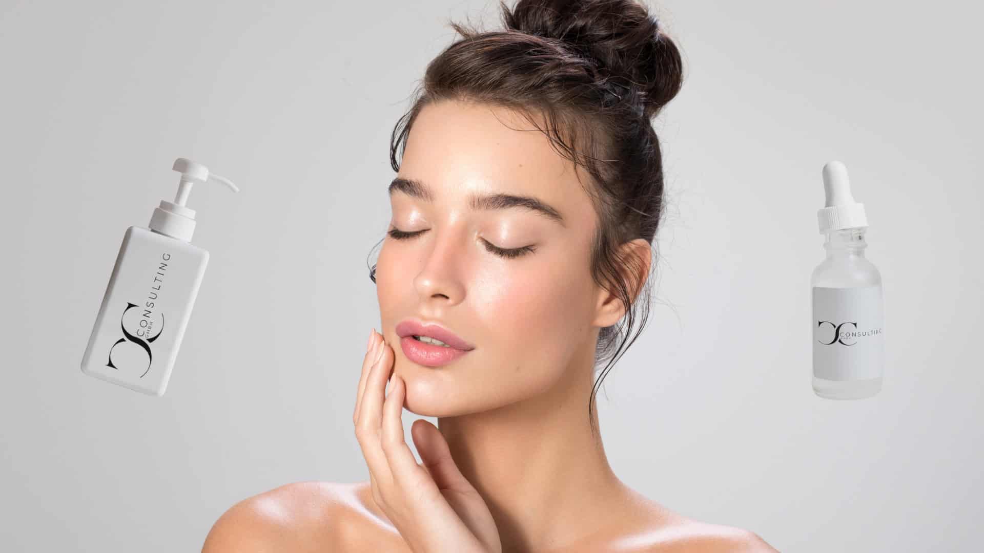 Junge Frau mit makelloser Haut und geschlossenem Blick berührt sanft ihr Gesicht. Links und rechts neben ihr schweben zwei Hautpflegeprodukte der Marke „CC Consulting GmbH“: ein Pumpspender und ein Serum mit Pipette.