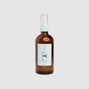 Braune Sprühflasche mit weißem Etikett und CC Consulting GmbH Logo, Produktbezeichnung „Hair Spray“, vor grauem Hintergrund.