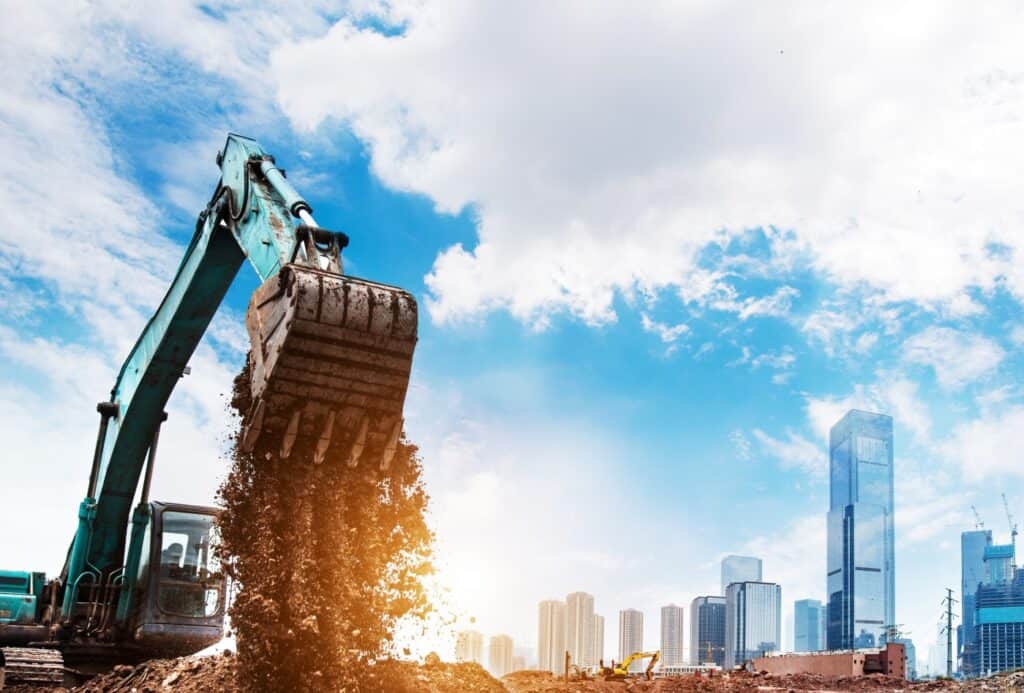 Ein großer Bagger kippt Erde auf einer Baustelle vor einer modernen Skyline mit Hochhäusern. Der Himmel ist blau mit weißen Wolken, die Szene symbolisiert urbanes Wachstum und Entwicklung.