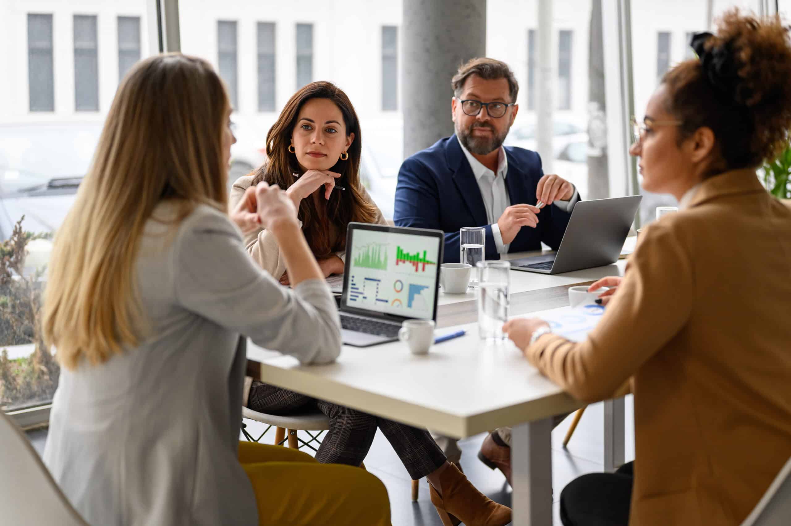 Businesswoman reviewing report on laptop while discussing business growth with coworkers in meeting
