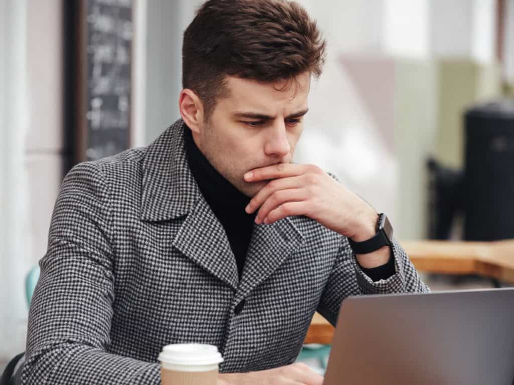 Nachdenklicher Unternehmer vor Laptop mit Kaffee – sinnbildlich für Unsicherheit beim Start eines Online-Shops.