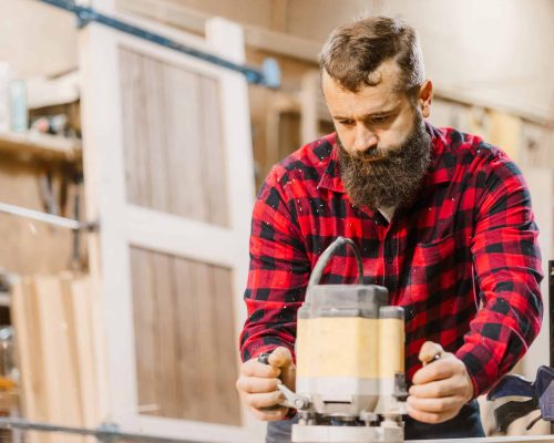 417594275 Carpenter uses router to craft wooden furniture in workshop during day